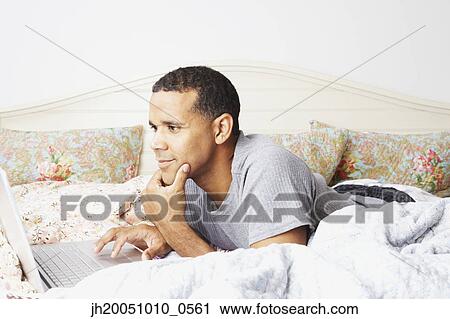 Man using a laptop in bed View Large Photo Image Stock Image - Man using a laptop in bed. Fotosearch