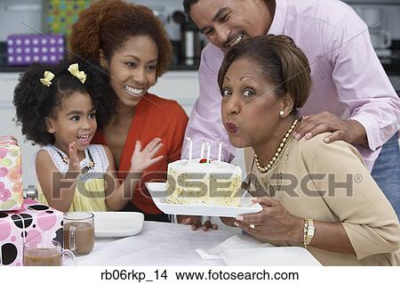 Picture - Mature woman blowing out the candles on her birthday cake. Fotosearch