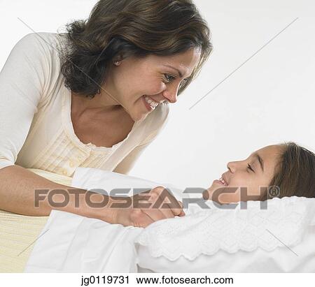 Stock Image - Mother tucking her daughter into bed. Fotosearch