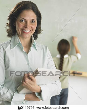 Stock Photograph - Teacher smiling for the camera as student works in the background. Fotosearch