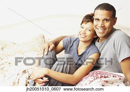 Young couple smiling for the camera in bed View Large Photo Image Stock Photo - Young couple smiling for the camera in bed. Fotosearch