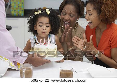 Stock Image - Young girl blowing out the candles on her birthday cake. Fotosearch