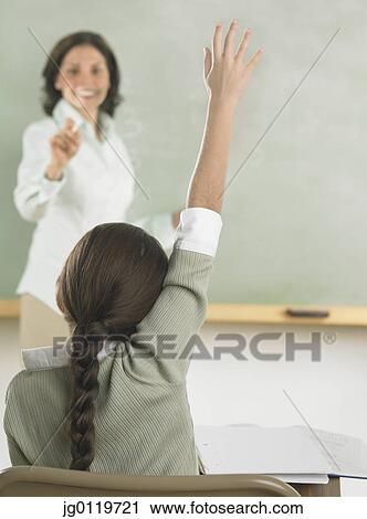 Stock Image - Young girl raising her hand in class. Fotosearch