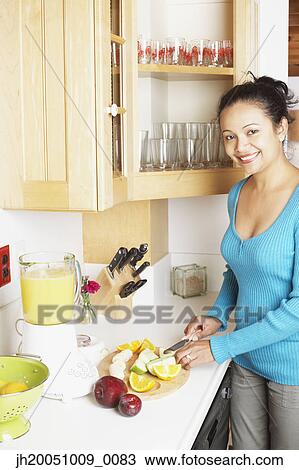 Stock Image - Young woman chopping fruit in the kitchen. Fotosearch