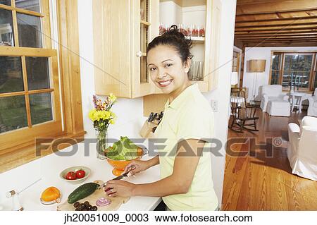 Stock Image - Young woman chopping vegetables in the kitchen. Fotosearch
