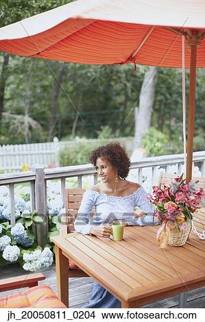 Picture - Young woman drinking a cup of coffee outdoors. Fotosearch