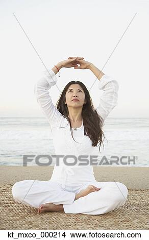 Picture - Young woman practising yoga on the beach. Fotosearch