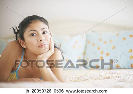 Stock Photograph - Young woman relaxing on her bed. Fotosearch