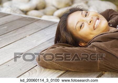 Stock Image - Young woman relaxing on wood deck. Fotosearch