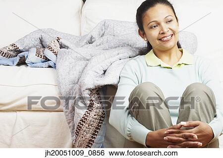 Stock Photograph - Young woman sitting against the couch. Fotosearch
