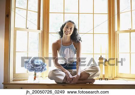 Young woman sitting cross-legged on a windowsill View Large Photo Image Stock Photo - Young woman sitting cross-legged on a windowsill. Fotosearch