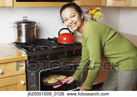 Young woman taking food out of the oven View Large Photo Image Stock Photograph - Young woman taking food out of the oven. Fotosearch