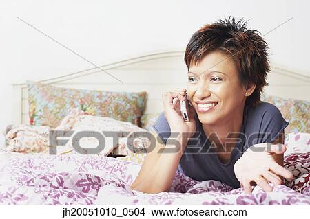 Picture - Young woman talking on her cell phone in bed. Fotosearch