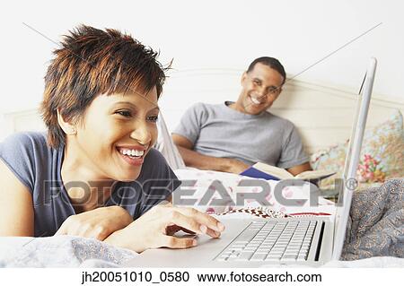 Stock Image - Young woman using a laptop in bed. Fotosearch