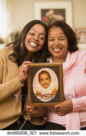 Stock Image - Mother and daughter displaying a baby picture. Fotosearch