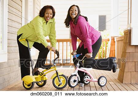 Stock Image - Mother and daughter riding tricycles on a porch. Fotosearch