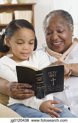 Stock Photo - Senior woman reading the Bible to her granddaughter. Fotosearch