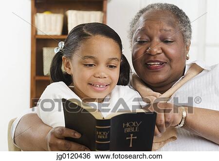 Stock Photograph - Senior woman reading the Bible to her granddaughter. Fotosearch