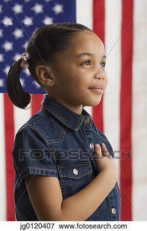 Stock Photo - Young girl holding her hand across her heart with American flag in background. Fotosearch