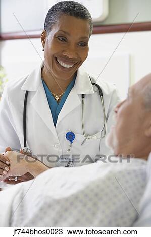 Stock Image - African female doctor holding patient's hand. Fotosearch