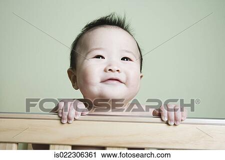 Stock Image - Asian baby smiling in crib. Fotosearch