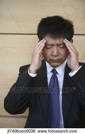 Stock Photograph - Asian businessman rubbing his temples. Fotosearch
