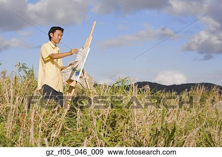 Stock Photo - Asian man painting at easel outdoors, Florianopolis, Brazil. Fotosearch