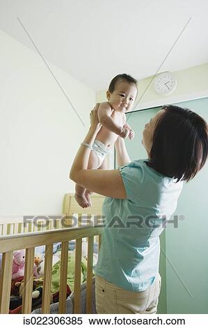 Asian mother lifting baby out of crib View Large Photo Image Stock Photography - Asian mother lifting baby out of crib. Fotosearch