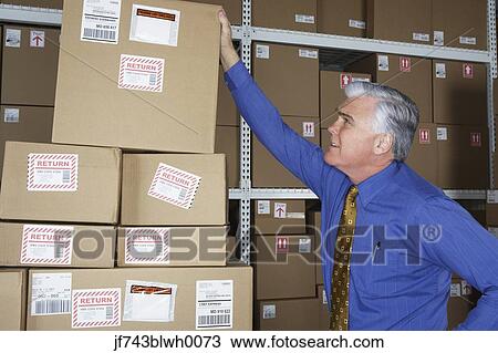 Stock Image - Businessman in warehouse looking at returned packages. Fotosearch
