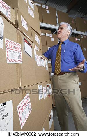 Stock Image - Businessman in warehouse looking at returned packages. Fotosearch
