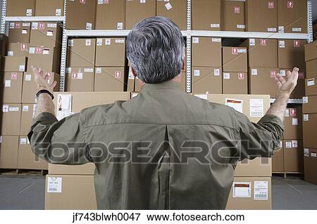 Stock Photo - Businessman in warehouse looking at stacks of packages. Fotosearch