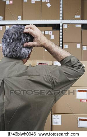 Stock Photograph - Businessman in warehouse scratching his head. Fotosearch