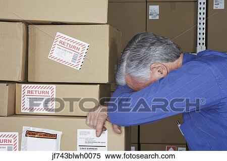 Stock Photography - Businessman in warehouse with head down on returned packages. Fotosearch