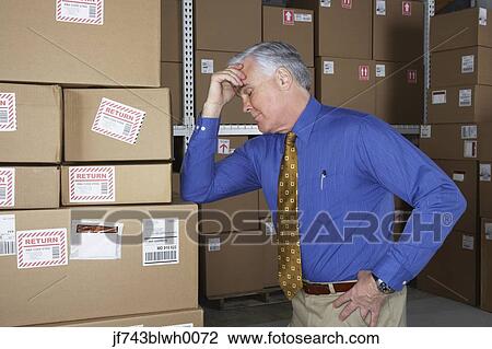 Stock Image - Businessman in warehouse with his head in his hand. Fotosearch
