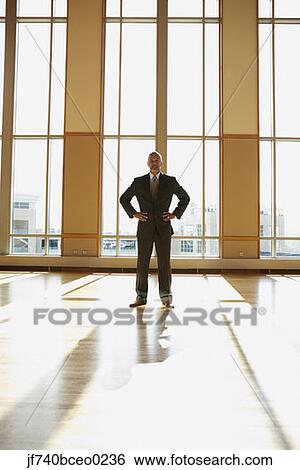 Stock Photograph - Businessman standing in sunlit room with hands on his hips, North Bethesda, Maryland, United States. Fotosearch