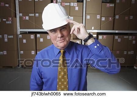 Businessman wearing hard hat and saluting in warehouse View Large Photo Image Stock Photography - Businessman wearing hard hat and saluting in warehouse. Fotosearch