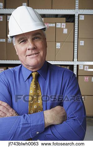 Stock Image - Businessman wearing hard hat in warehouse. Fotosearch