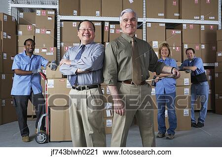 Stock Image - Businessmen with warehouse workers in warehouse. Fotosearch