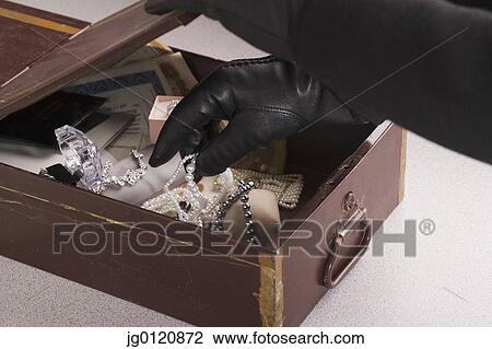 Stock Image - Close up of gloved hands taking jewels out of box. Fotosearch