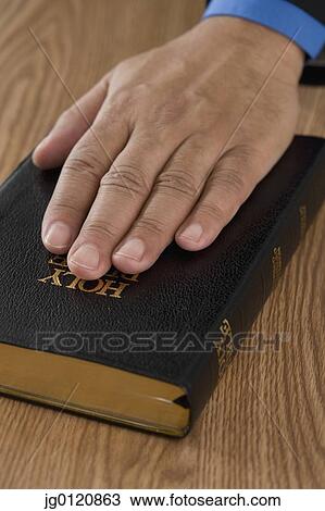 Stock Image - Close up of male hand on bible. Fotosearch