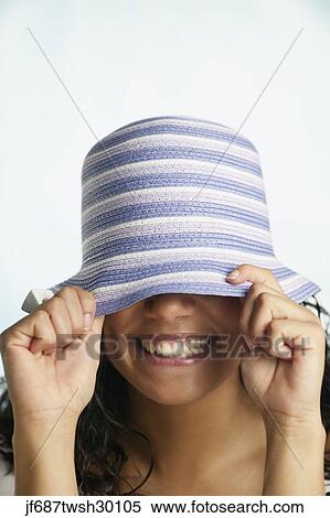 Stock Photography - Close up of woman smiling while pulling hat down over her eyes. Fotosearch