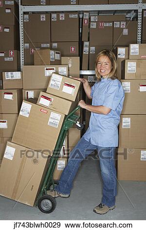 Stock Photo - Female warehouse worker using hand truck. Fotosearch