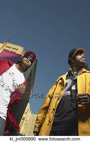 Stock Image - Low angle view of two young African men standing in urban area, Oakland, California, United States. Fotosearch