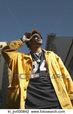 Stock Image - Low angle view of young African man standing in urban area, Oakland, California, United States. Fotosearch