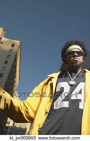 Stock Image - Low angle view of young African man standing in urban area, Oakland, California, United States. Fotosearch