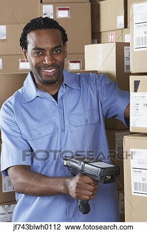 Stock Image - Male African warehouse worker scanning packages. Fotosearch