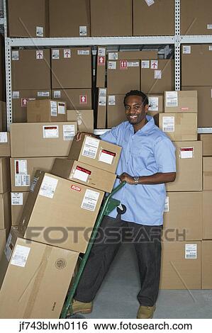 Stock Photograph - Male African warehouse worker using hand truck. Fotosearch