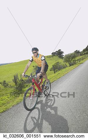 Stock Image - Male cyclist riding on rural road, California, United States. Fotosearch