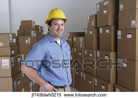 Stock Photography - Male warehouse worker wearing hard hat in warehouse. Fotosearch