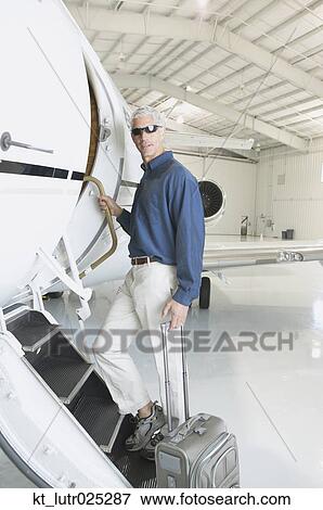 Man with suitcase boarding airplane in hanger, Nobato, California, United States View Large Photo Image Stock Photo - Man with suitcase boarding airplane in hanger, Nobato, California, United States. Fotosearch